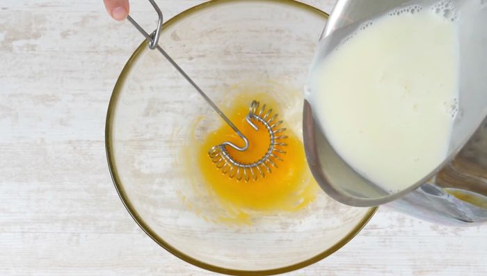 Die heiße Milch-Sahne-Mischung langsam und unter ständigem Rühren zum Eigelb geben.
