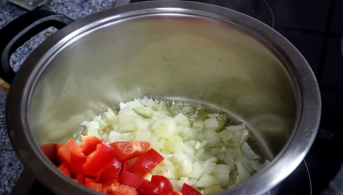 Zwiebel und Knoblauch klein schneiden und mit etwas Olivenöl in einem Topf anbraten. Rote, gelbe und grüne Paprika klein schneiden und hinzufügen.