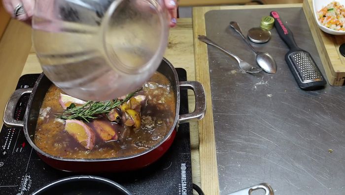 Rotwein, Bouillon und Wasser hinzufügen. Alles ca. 1 Stunde köcheln lassen.