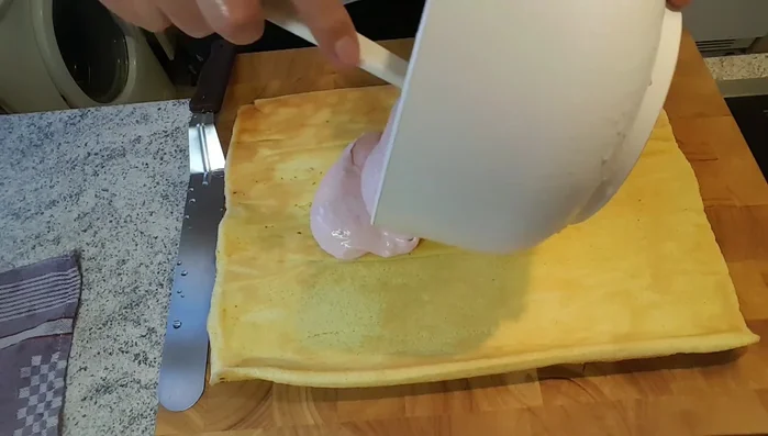 Die Himbeercreme gleichmäßig auf dem Biskuit verteilen und vorsichtig aufrollen.