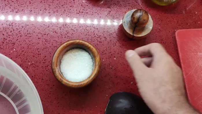 Aubergine in kaltes Salzwasser geben und mindestens 30 Minuten einweichen lassen, um Bitterstoffe zu entfernen.