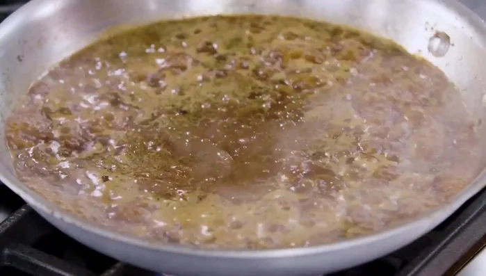 Die Brühe in die Pfanne geben, die Hitze auf mittlere bis hohe Stufe erhöhen und zum Kochen bringen. Die Soße etwa 5 Minuten lang kochen lassen, bis sie leicht eingekocht ist. Dabei darauf achten, dass alle braunen Reste vom Boden und den Seiten der Pfanne abgekratzt und wieder in die Soße eingerührt werden.