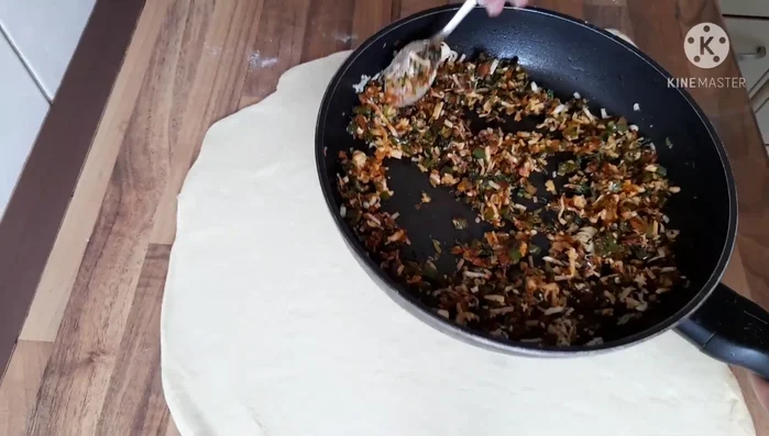 Paprika-Zwiebel-Füllung mit Käse auf einen Teigfladen verteilen, einrollen (321.289).