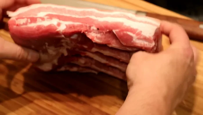 Schweinebauch vorbereiten: Knochen und Knorpel aus dem Schweinebauch entfernen. Die Haut einschneiden und das Fleisch in Würfel schneiden.