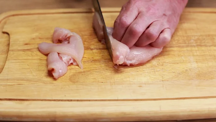 Hähnchenbrustfilet in kleine Stücke schneiden und mit Pfeffer und Salz würzen. Das gewürzte Fleisch über die Kartoffeln geben.