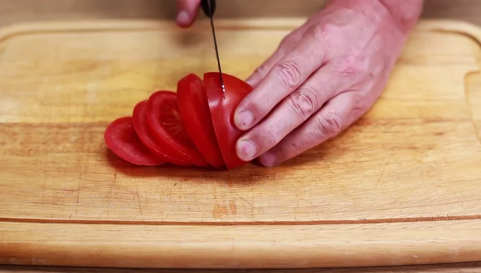 Tomaten waschen und in Scheiben schneiden. Nach 30 Minuten die Form aus dem Ofen nehmen, abdecken und mit geriebenem Käse bestreuen.