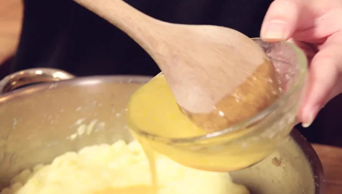 Eigelb, geschmolzene Butter (abgekühlt), Kartoffelmehl, Muskat und Salz zu den Kartoffelpüree geben und gut vermischen, bis ein gleichmäßiger Teig entsteht.