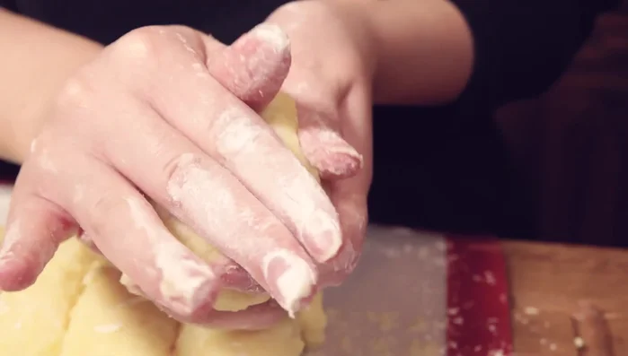 Jedes Teigstück platt drücken, einen Käsewürfel in die Mitte geben und den Knödel verschließen. Hände dabei mit Mehl bestäuben.