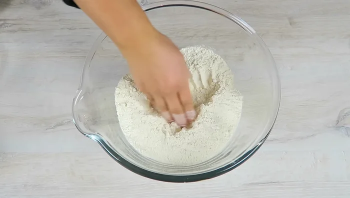 Mehl in eine große Schüssel geben und eine Mulde formen. Hefe zerbröseln, in die Mulde geben und mit etwas Zucker bestreuen. Die Hälfte der Milch hinzufügen, abdecken und 10-15 Minuten ruhen lassen, bis die Hefe schäumt.