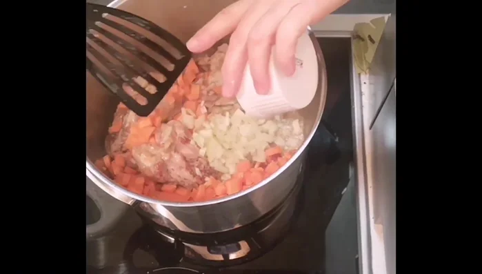 Möhren, Zwiebeln, Knoblauch, Salz, Pfeffer und Lorbeerblätter hinzufügen und anbraten.