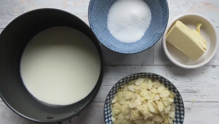 Für den Mandelbelag: Sahne, Butter, gehobelte Mandeln und Zucker (außer 2 Mandeln) in einem Topf schmelzen. Vom Herd nehmen, kurz abkühlen lassen und die restlichen Mandeln unterrühren.
