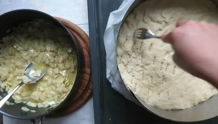 Mit einer Gabel Löcher in den Teig stechen. Den Mandelbelag gleichmäßig verteilen.