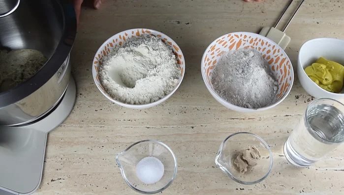 Sauerteig (350g) aus dem Vortag verwenden. Weizenmehl (300g), Roggenmehl (150g), Salz (10g), Hefe (15g, optional) und lauwarmes Wasser (250ml) in einer Schüssel vermischen.