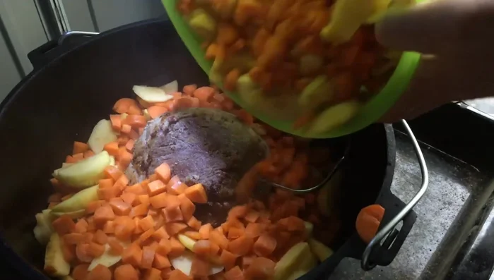 Nach 3-4 Minuten Karotten und Äpfel hinzufügen, das Fleisch leicht anheben, damit es auf der Mischung liegt.