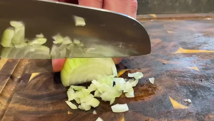 Zwiebel halbieren und in feine Würfel schneiden (153.25, 156.37, 159.94). In der Pfanne mit etwas Butter anschwitzen (166).