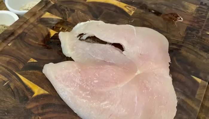 Hähnchenschnitzel mit dem Messer halbieren und einen Butterfly-Schnitt durchführen (28.05). Schnitzel mit Klarsichtfolie bedecken und mit dem Hammer leicht plattieren (30.599, 40.91, 44.7).