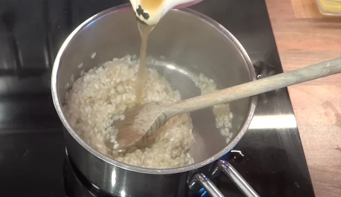 Mit heißer Gemüsebrühe nach und nach aufgießen und unter ständigem Rühren köcheln lassen, bis der Reis gar ist (ca. 10 Minuten).