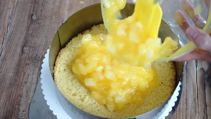 Einen Biskuitboden in den Tortenring legen, Birnenpudding darauf verteilen, zweiten Boden daraufsetzen.