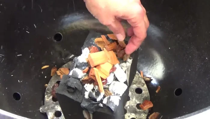 Apfelchips auf die glühende Holzkohle legen, Wasserschalen und Grillroste in den Grill stellen. (195.55)