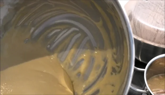 Spätzleteig durch eine Kartoffelpresse drücken, um Spätzle herzustellen.