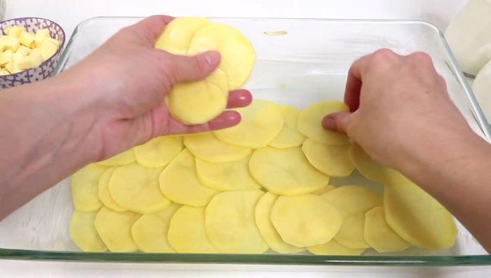 Kartoffelscheiben auf dem Boden der Auflaufform verteilen, salzen, pfeffern und mit Butterflocken bestreuen.