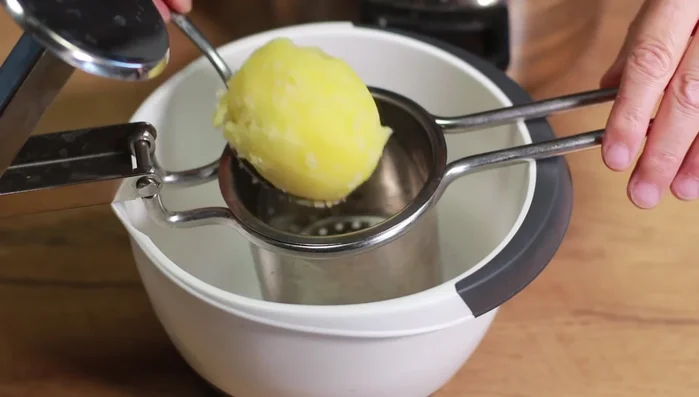Gekochte Kartoffeln durch eine Kartoffelpresse drücken.
