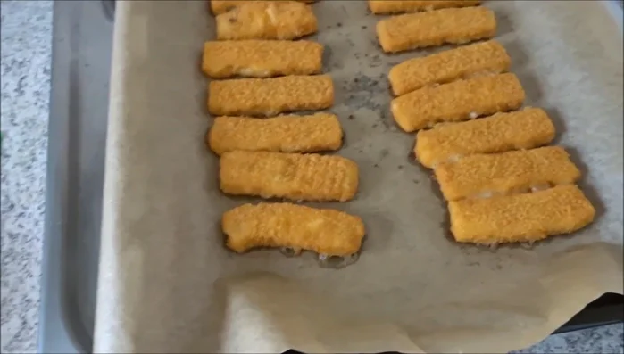 Fertige Fischstäbchen mit einer Zange vorsichtig vom Backblech nehmen und auf einen Teller legen.