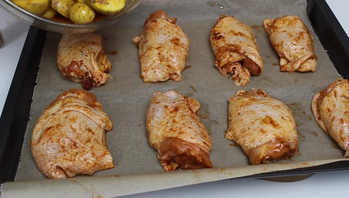 Hähnchenkeulen und Kartoffeln auf ein Backblech legen. Die Kartoffeln in die Lücken zwischen den Keulen geben.